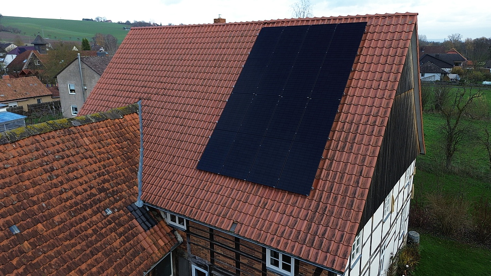Drohnenaufnahme von Fachwerkhaus mit mit Photovoltaikanlage auf dem roten Ziegeldach, seitlich