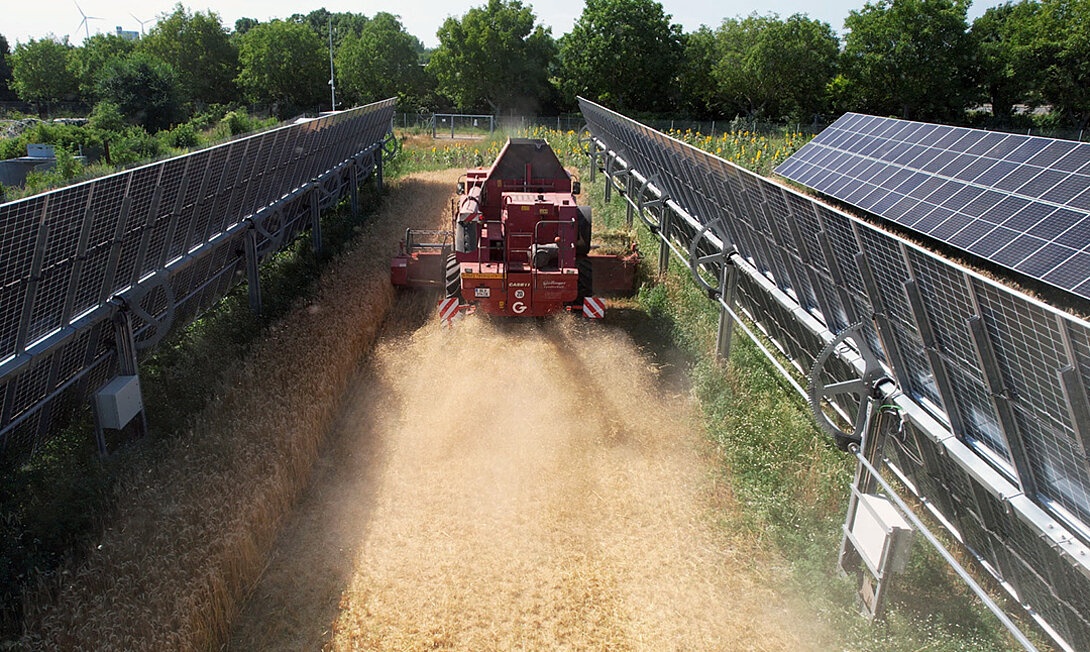 Landmaschine fährt durch hochgeklappte Photovolatikanlagen auf dem Feld, 