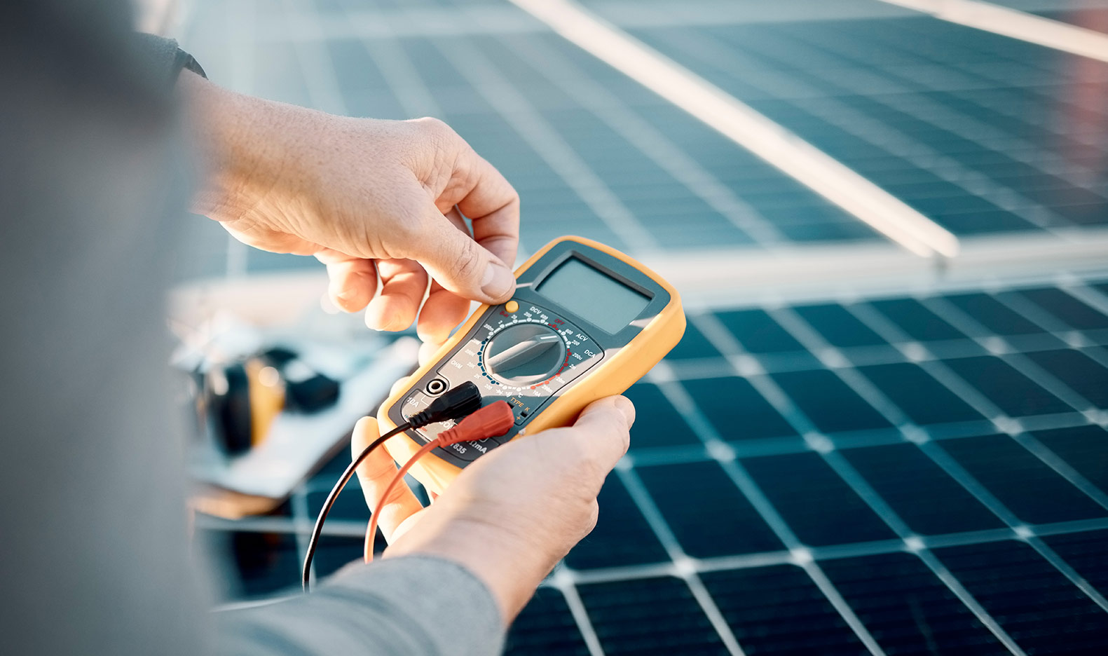 Zwei Hände halten ein Messgerät, im Hintergrund Photovoltaik Module